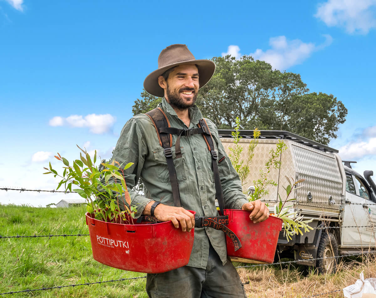 Support livelihoods - man smiling holding tree saplings